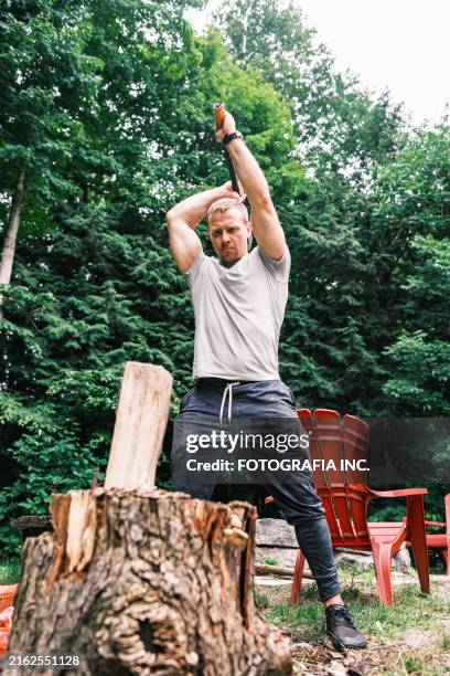 young man chopping wood with axe - bijl stockfoto's en -beelden