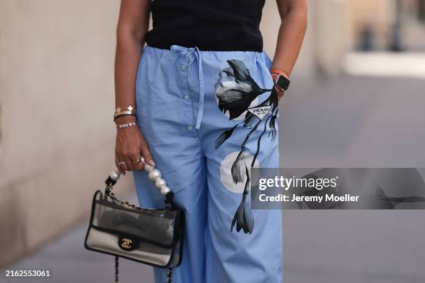 Karin Teigl is seen wearing a black top from Zara; blue wide pajama pants with black floral print from Prada; several rings in gold and silver;...