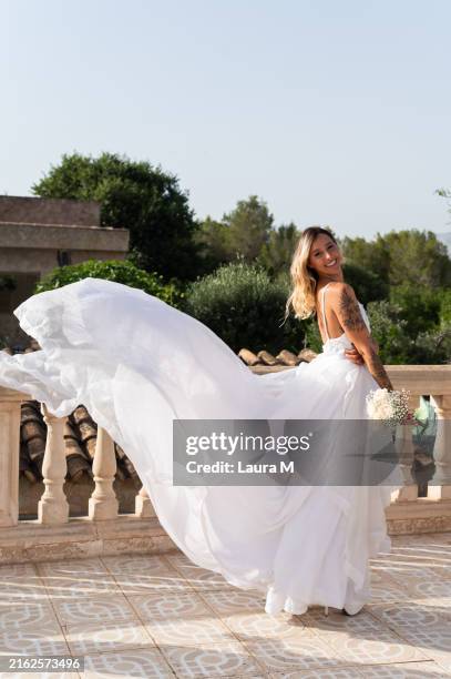 bride holding bouquet with flowing dress posing on balcony - wedding dress stock pictures, royalty-free photos & images