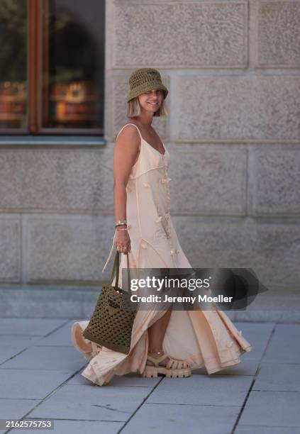 Karin Teigl is seen wearing a woven raffia hat in olive from Prada; a yellow-gold “Alhambra” necklace with green pendant in cloverleaf shape from Van...