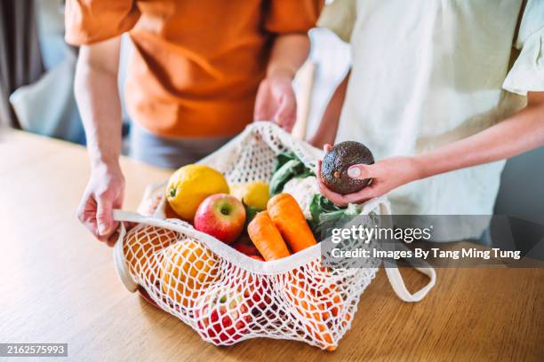 close-up of mother and daughter unpacking fresh fruits and vegetables together in kitchen - vegetable stock pictures, royalty-free photos & images