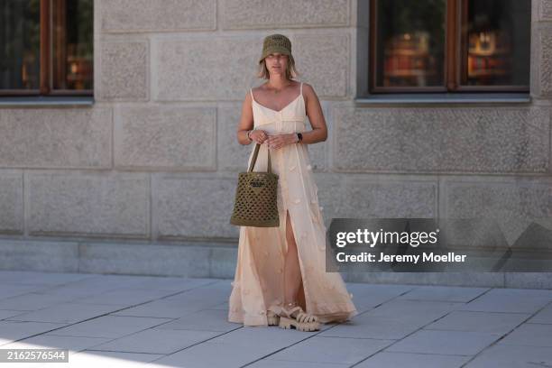 Karin Teigl is seen wearing a woven raffia hat in olive from Prada; a yellow-gold “Alhambra” necklace with green pendant in cloverleaf shape from Van...