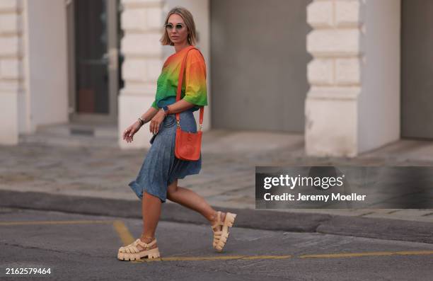Karin Teigl is seen wearing geometric sunglasses with golden frame; a cropped tee with a round neckline, elbow-length sleeves, and a color gradient...