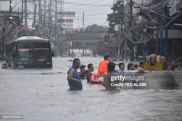 People wade through the flood waters past a half-submerged passenger bus along a street in Manila on July 24, 2024 amid heavy rains brought by...