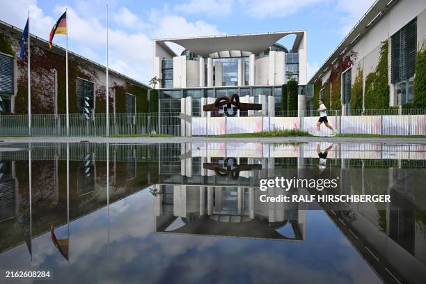 Jogger runs passed the Chancellery building under a blue sky as a reflection of them is seen on a puddle on July 24 in Berlin.