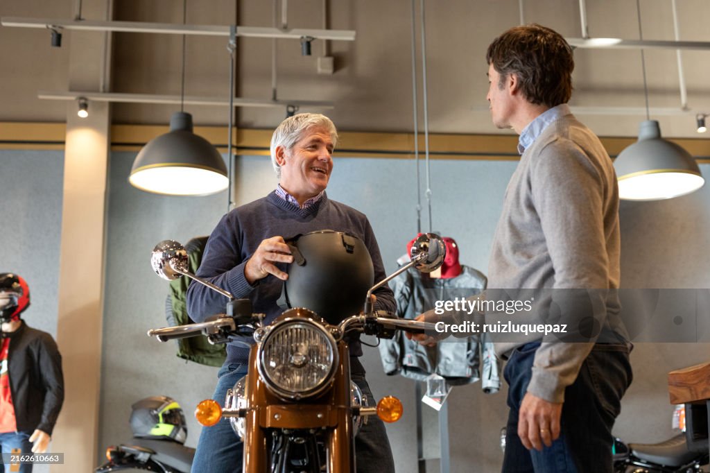 Two mature men shopping motorcycles, helmets and clothing in a motorcycle store