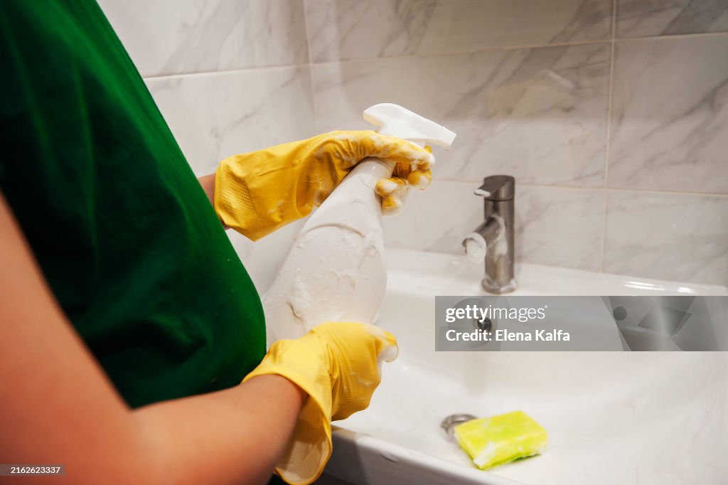 A hand in protective rubber gloves is seen wiping and cleaning the sink in the bathroom