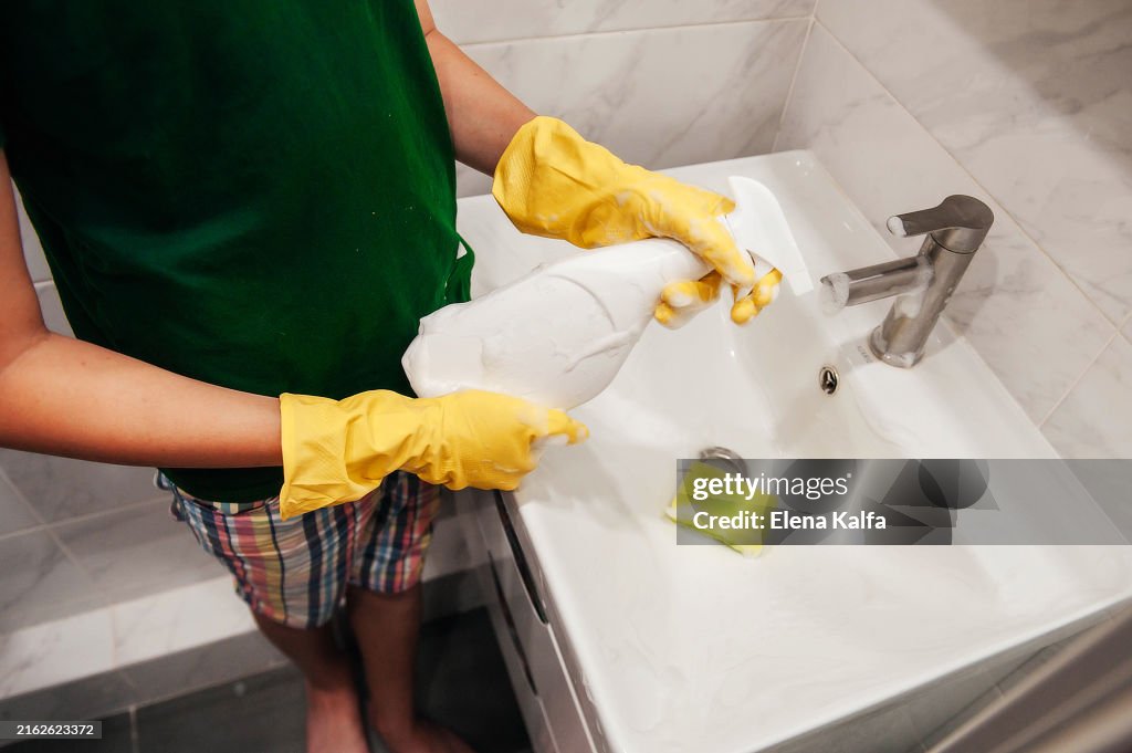 A hand in protective rubber gloves is seen wiping and cleaning the sink in the bathroom