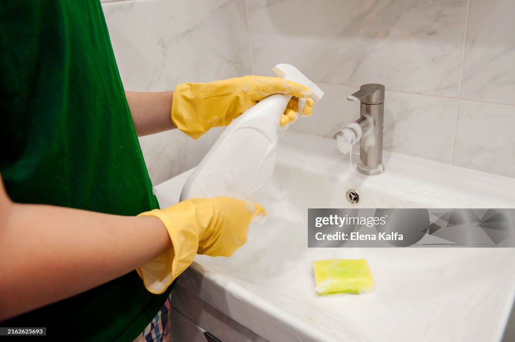 A hand in protective rubber gloves is seen wiping and cleaning the sink in the bathroom