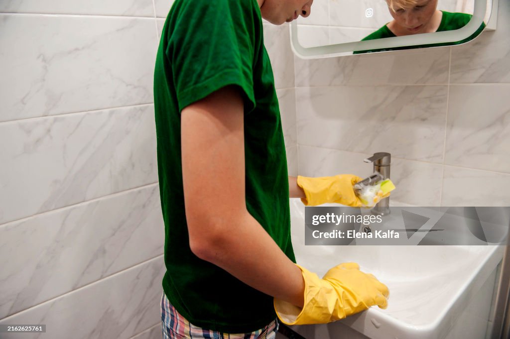 A hand in protective rubber gloves is seen wiping and cleaning the sink in the bathroom