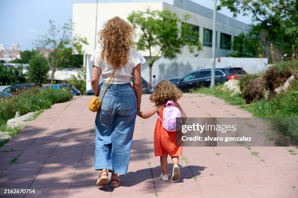 mother walking daughter to school on a sunny day - girls holding hands stock pictures, royalty-free photos & images