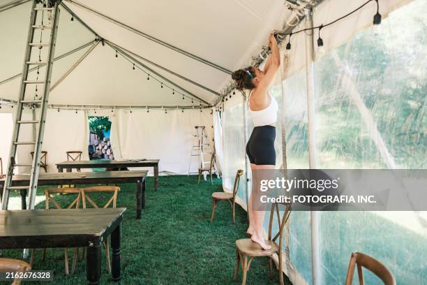 young woman decorating lights inside wedding reception tent - setting up tent stock pictures, royalty-free photos & images