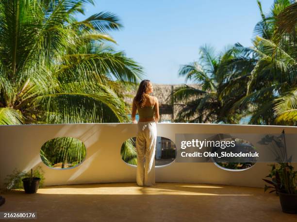 elegant woman on the balcony at sunset looking at palm trees on tourist resort - luxury women stock pictures, royalty-free photos & images