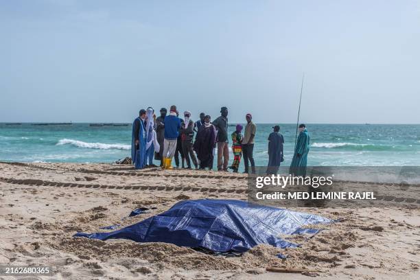Bystanders look at covered bodies of migrants who perished in a shipwreck off the coast of Mauritania while on a beach outside Nouakchott on July 24,...