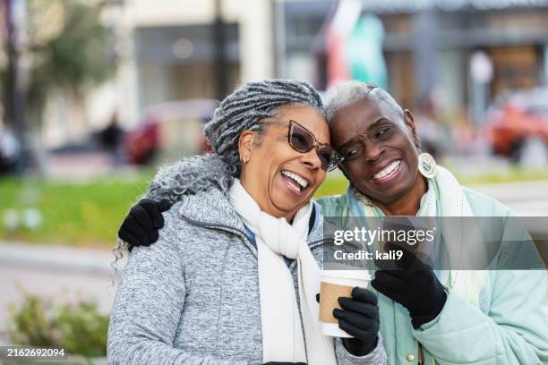 des femmes noires âgées en vêtements chauds avec du café, riant - paire de gants noirs photos et images de collection