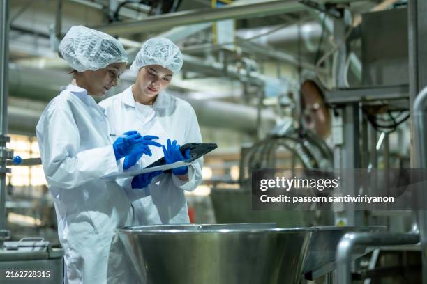 zwei wissenschaftler mit schutzausrüstung und handschuhen mit einem digitalen tablet in einer industriellen laborumgebung. - abfüllanlage stock-fotos und bilder