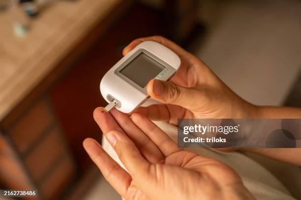 woman with glucometer checking blood sugar level at home - glucose stockfoto's en -beelden