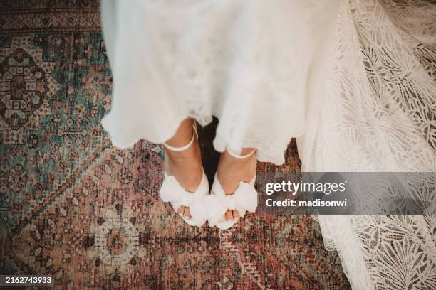 mariée en robe de mariée enfilant ses chaussures à talons hauts avant la cérémonie - robe de mariée photos et images de collection