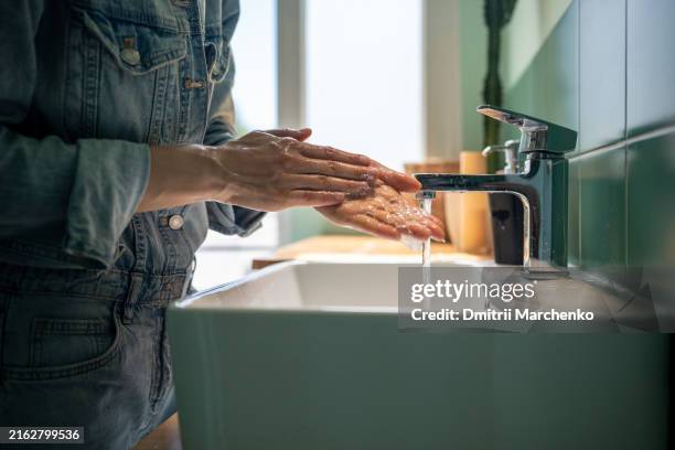 unrecognizable woman washes hands with soap and foam in the sink on sunny day in bright bathroom - ossessivo foto e immagini stock
