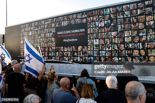People stand near a wall covered with pictures of Israeli hostages held by Palestinian Hamas militants in the Gaza Strip since the October 7 attacks,...