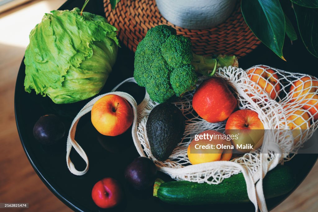 Fresh organic fruits and vegetables in reusable mesh bag on kitchen at home