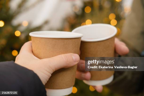 couple holding paper glasses with hot drinks at the christmas market - takeaway coffee stock pictures, royalty-free photos & images