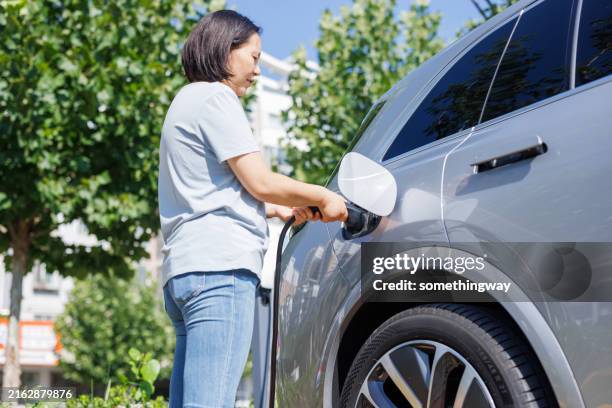 women inserts a power cord into an electric car for charging - elkontakt bildbanksfoton och bilder