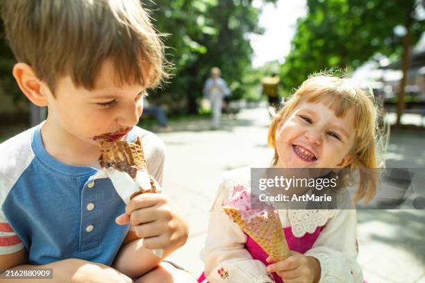 cute children enjoying ice-cream in summer park - boy and girl eating ice cream stock-fotos und bilder