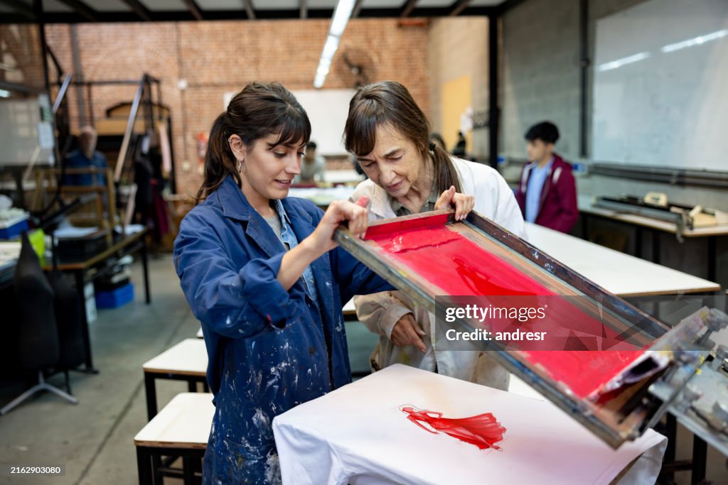 Student printing a design on a textile and showing her teacher in a fashion class