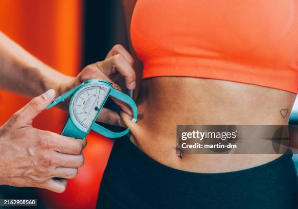 entrenador que mide la grasa corporal de la mujer con caliper - calibrador fotografías e imágenes de stock