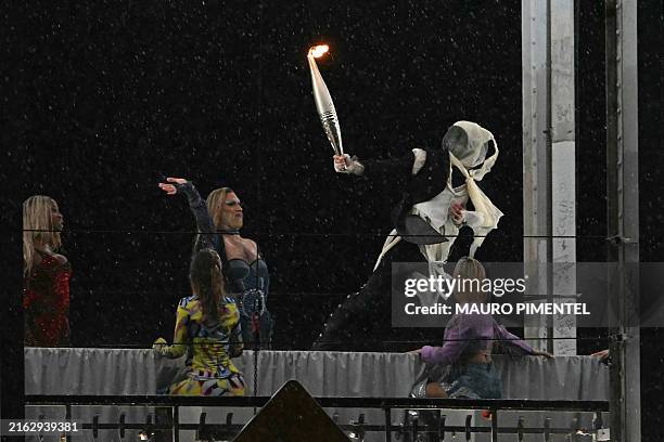 Torchbearer moves past models on a catwalk erected along the Passerelle Debilly bridge along the Seine river during the opening ceremony of the Paris...