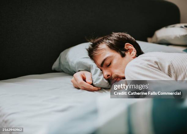 a man lies on his front, snuggled into a pillow, in an exhausted state - china foto e immagini stock