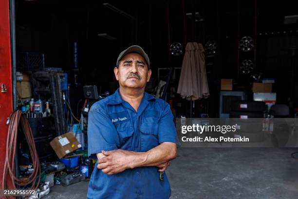seasoned mechanic exudes expertise in well-equipped auto repair shop. latino repairman stands confidently amid tools and car parts. - mexican american stock pictures, royalty-free photos & images