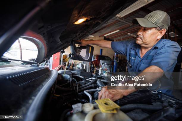 engine oil change. middle-aged latino mechanic diligently inspects car motor. - mexican american stock pictures, royalty-free photos & images