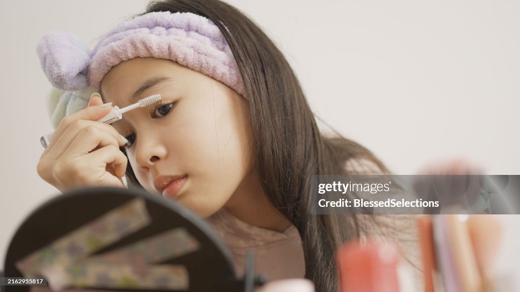 Mixed Asian preteen girl using lash and brown comb at home, beauty vlogger, self-love concept