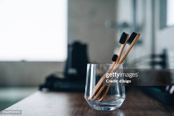 eco-friendly plastic free wooden family toothbrushes in a glass cup on a bathroom table top. zero waste concept. symbolize family life. family love and togetherness - brosse à dents photos et images de collection