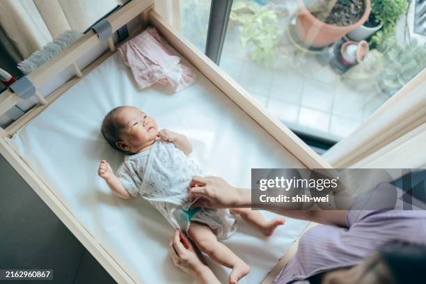 a baby girl is lying on the changing table while her mother is changing her clothes, performing infant care and grooming tasks. - changing diaper stock pictures, royalty-free photos & images