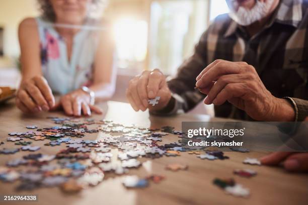 close up of mature couple playing with jigsaw puzzles at home. - puzzel stockfoto's en -beelden
