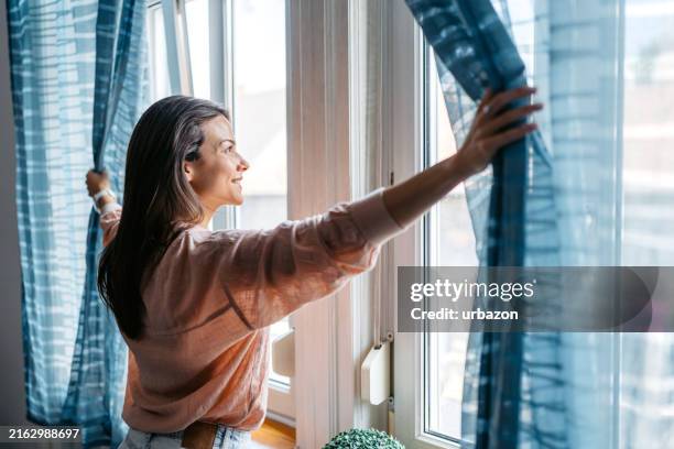 mujer joven abriendo las cortinas en el dormitorio en budapest por la mañana - apertura fotografías e imágenes de stock