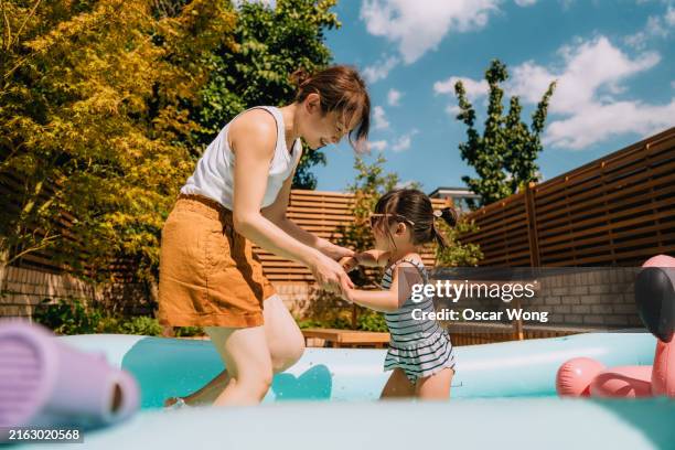 young asian mother having fun with her toddler daughter in inflatable swimming pool in backyard - family staycation stock pictures, royalty-free photos & images