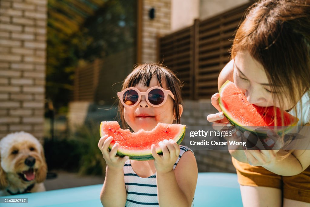 Young Asian toddler girl refreshing with watermelon slice with her mother in backyard