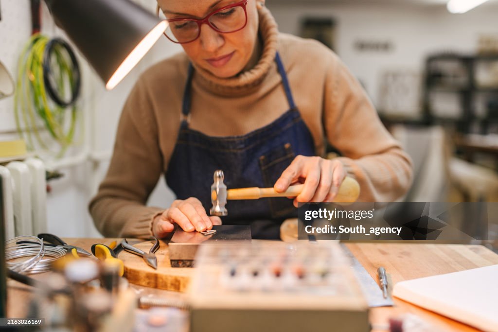 Handwerkliches Basteln von Schmuck mit Hammer auf einer Werkbank