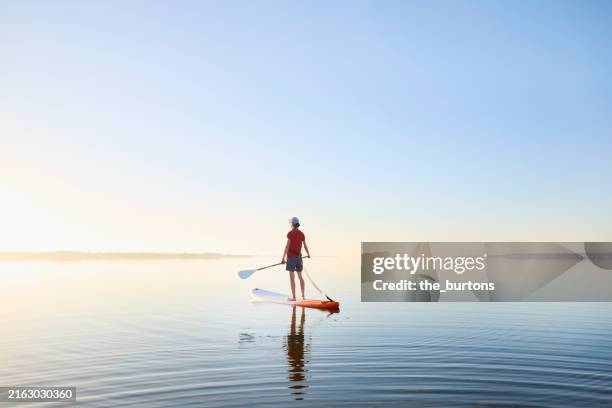a woman stands on a paddle board by the sea at idyllic sunrise - estabilidad fotografías e imágenes de stock