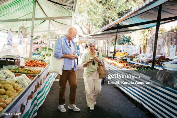 senior-paar probiert tropische früchte auf dem straßenmarkt - gemeinsam gehen stock-fotos und bilder