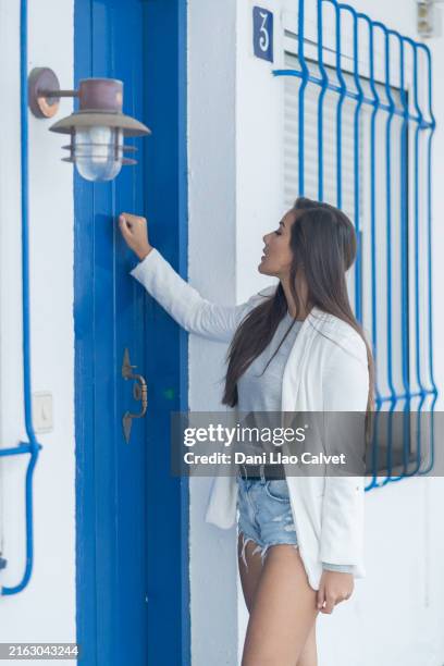 ragazza vestita con una giacca bianca che bussa a una porta blu - bussare foto e immagini stock