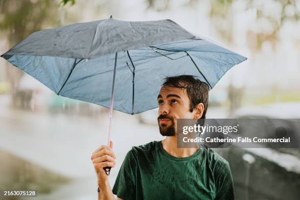 an irritated young man gets caught in the rain with a broken umbrella - bad luck stock pictures, royalty-free photos & images