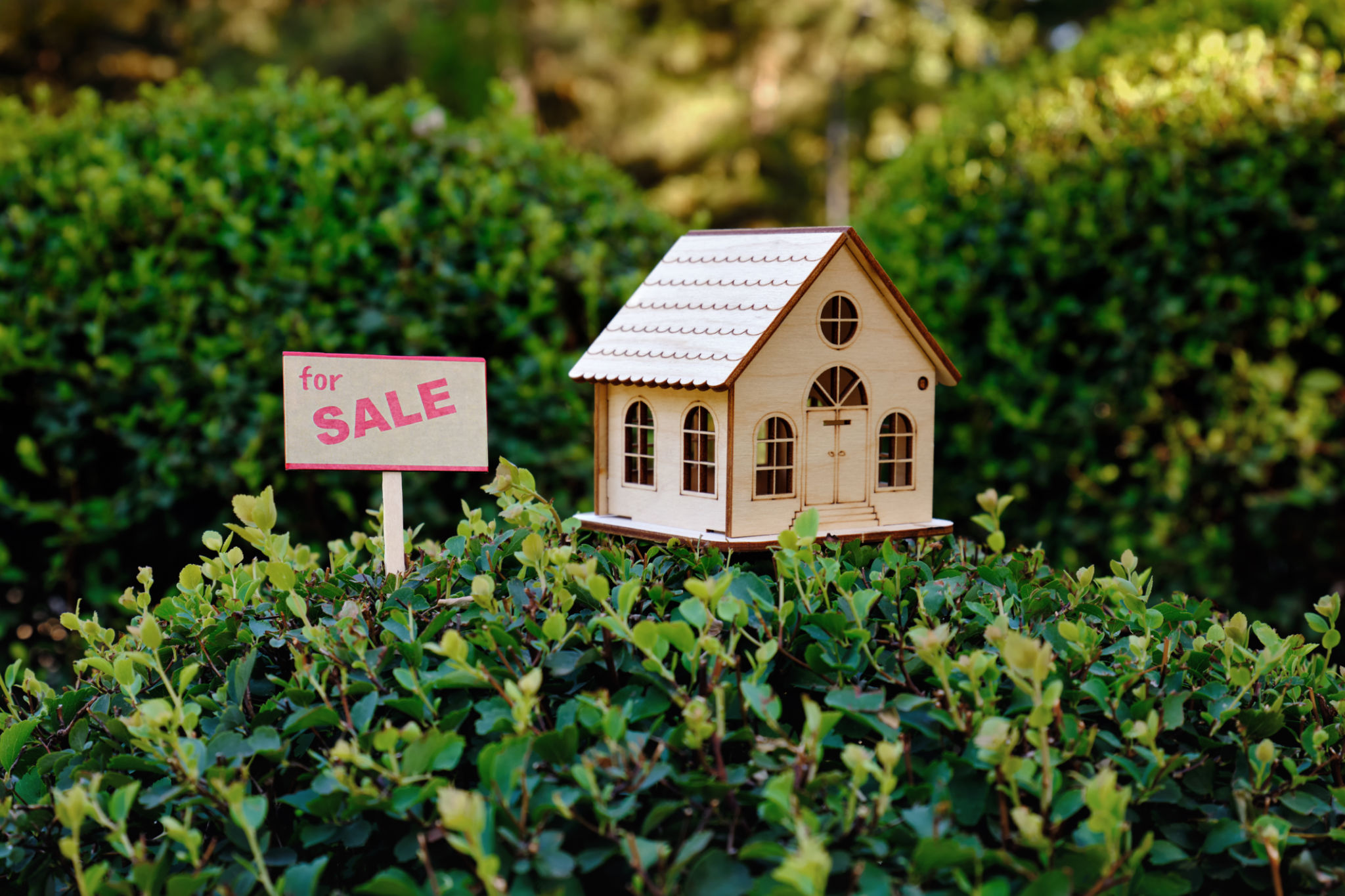 Small a sign. House for sale. A miniature composition with a toy wooden house with green grass. Small a sign. House for sale. A miniature composition with a toy wooden house with green grass.