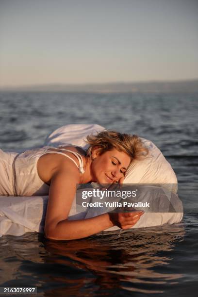 woman relaxing on mattress floating bed in ocean at sunset - floating on water stock pictures, royalty-free photos & images