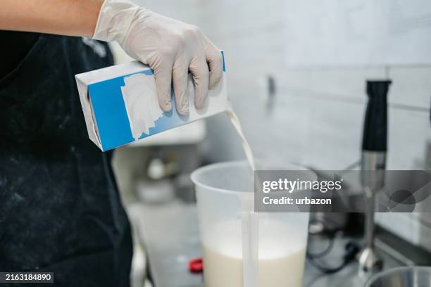 young man pouring milk to make ice cream batter in an ice cream shop - ice cream maker stock pictures, royalty-free photos & images