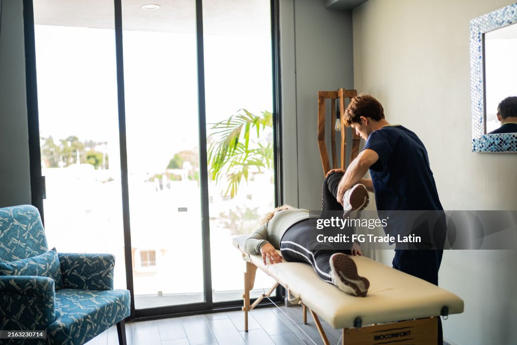 Young physiotherapist stretching mature patient woman during consultation at house call